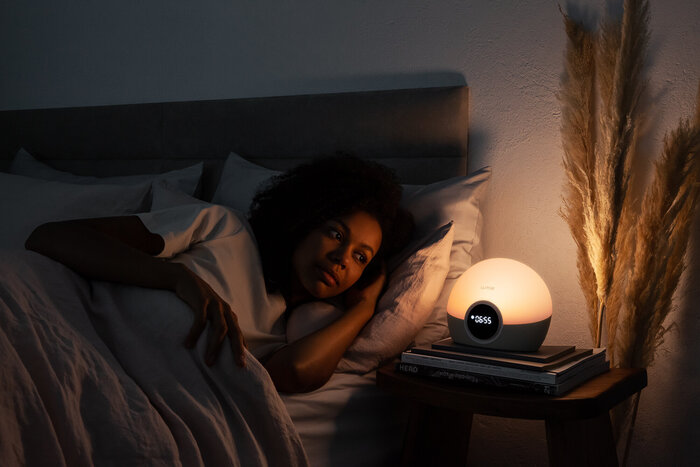 woman lying in bed in a dark room looking at a digital lamp next to her with a clock on it