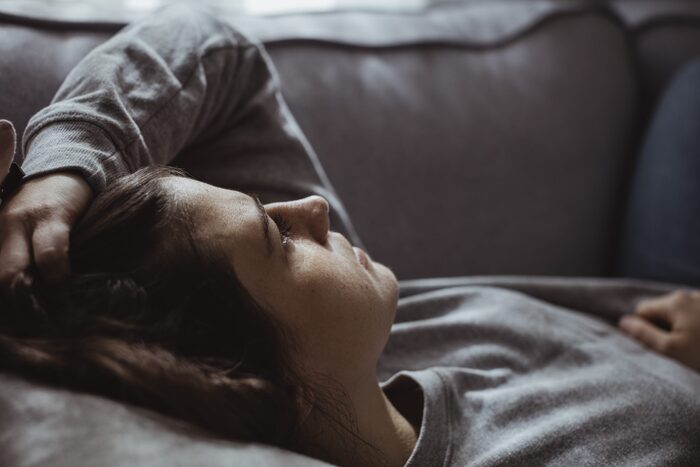 close up of a woman dressed in gray relaxing on a couch with her hand in her hair looking outside through the window