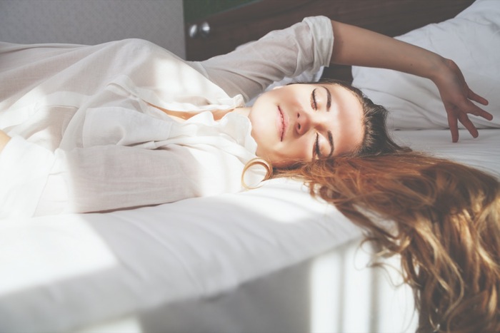 woman dressed in white waking up with her long hair on the bed