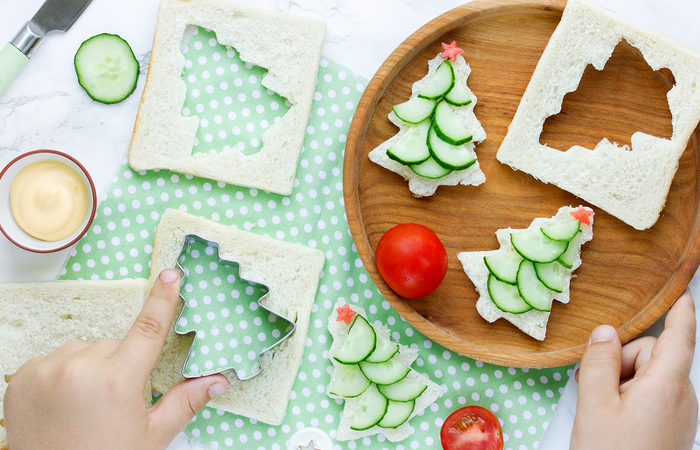 holiday food christmas tree shaped sandwiches with tomatoes and cucumber child making them and putting them on a wooden plate