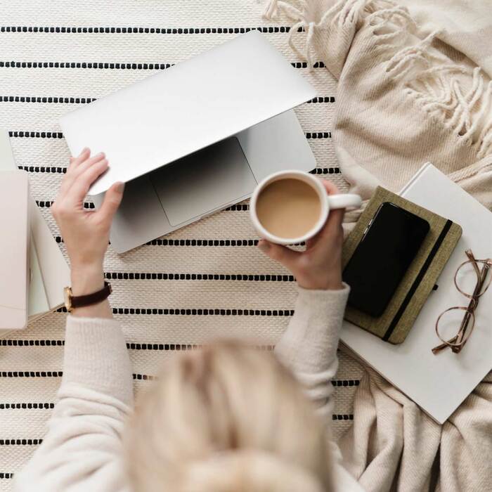 a back of a blond woman on a striped floor with her laptop holding a cup of coffee