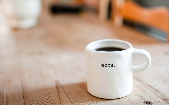 white mug with the word begin written in black on it sitting on a wooden table