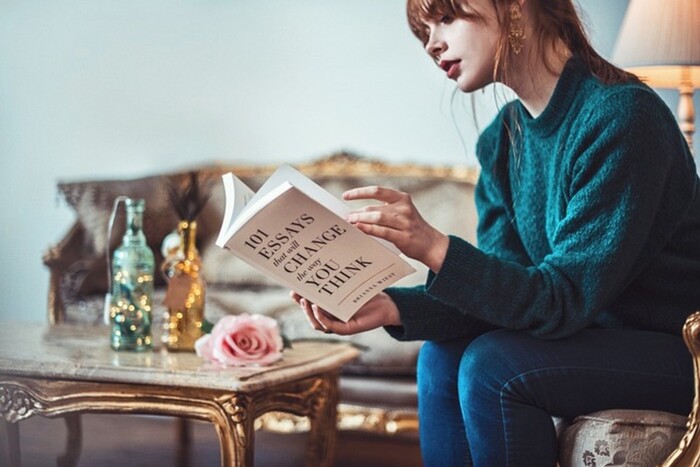 artistic photography of a woman sitting in an elegant room dressed in a green top and jeans reading a book 