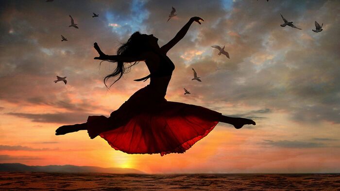 woman in a red dress dancing and jumping in the air shot at sunset with birds flying around