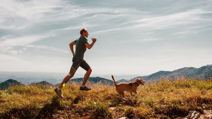 tall man jogging outdoors in a mountain with his dog on a sunny day