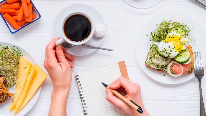 woman's hands on a table writing in a notebook with a salty breakfast and a cup of coffee