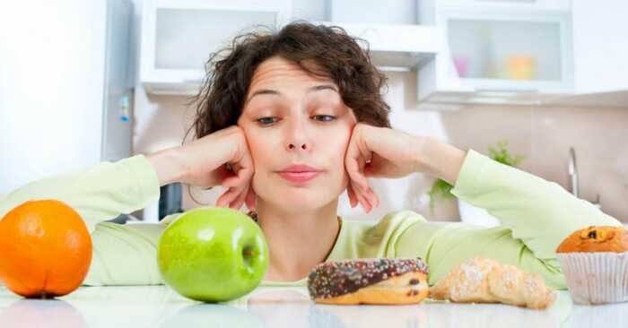 healthy choices woman on a kitchen table choosing between unhealthy and healthy food options