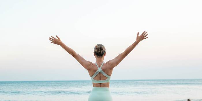 healthy habits woman in sportswear outside with her hands up looking at the sea