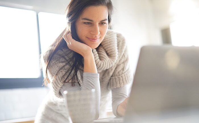 woman in a sweater in a light spacious room looking into her computer screen and smiling