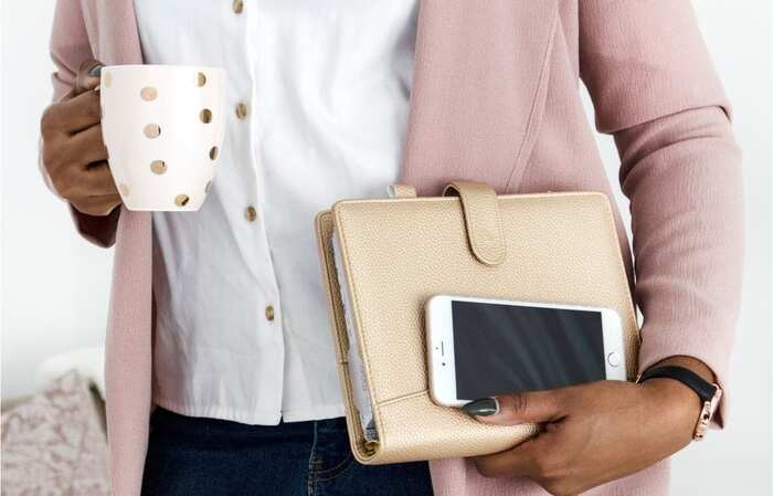 woman with a cute coffee cup holding a planner and a phone dressed in a pink