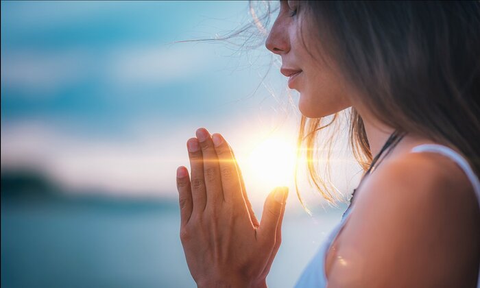 woman praying with her hands together in prayer at sunrise