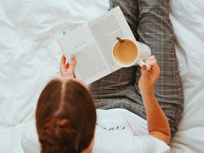 reading a book in bed woman sitting in bed with a coffee cup 