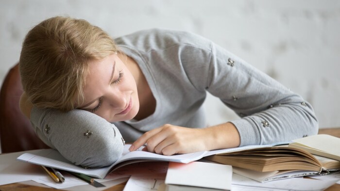 woman in her pajama sleeping over a pile of textbooks