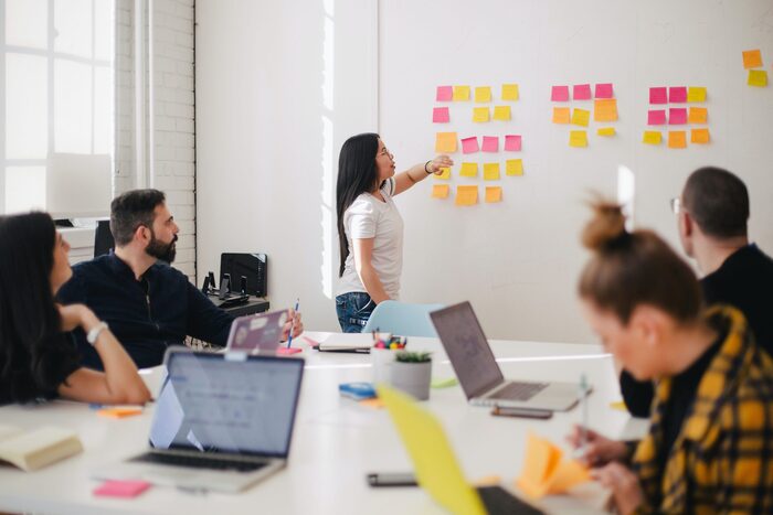 strategies for decision making woman placing colorful sticky notes on a white board in front of her team of cowerkers