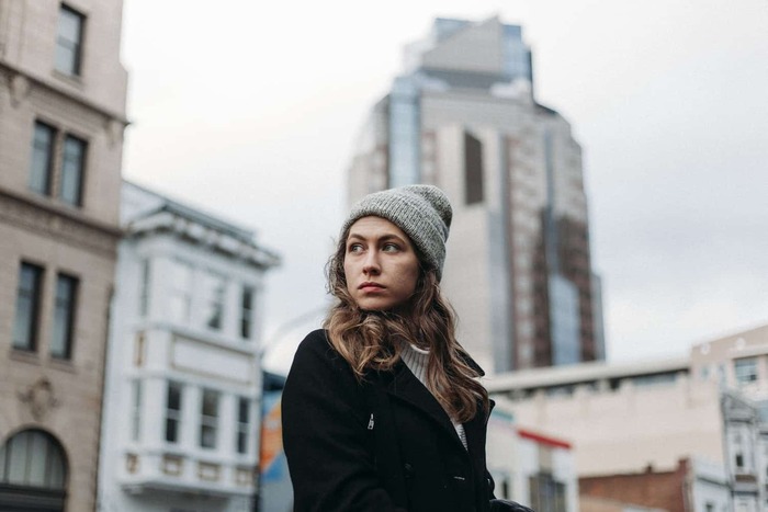 woman out in the city dressed in a hat and a black coat looking around