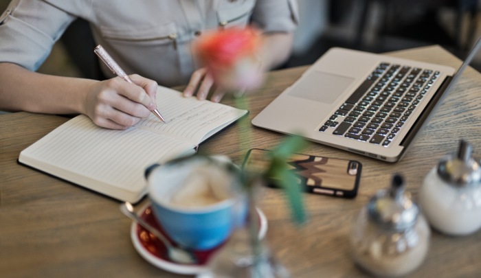 update routines person on a table in a coffee writing in their notebook and computer