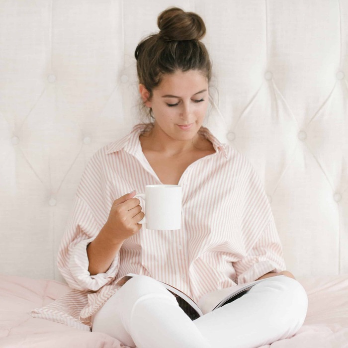 woman in her pajama chilling and reading a book with a white tea mug in her hand and her hair up