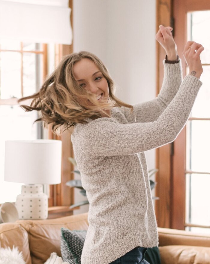 woman dancing at home with a sweater on smiling and looking at the camera