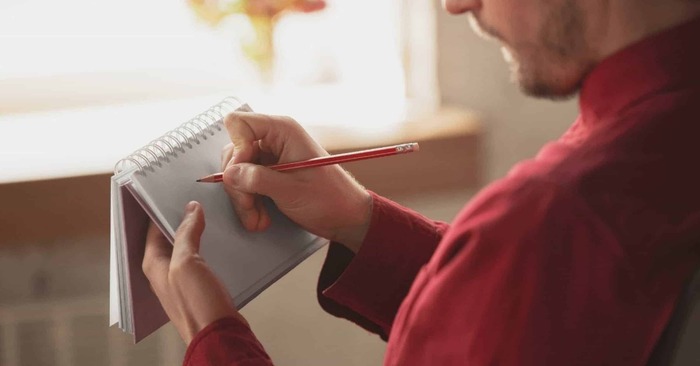 writing things down close up of a man with red shirt in front of a window writing down notes in a notebook