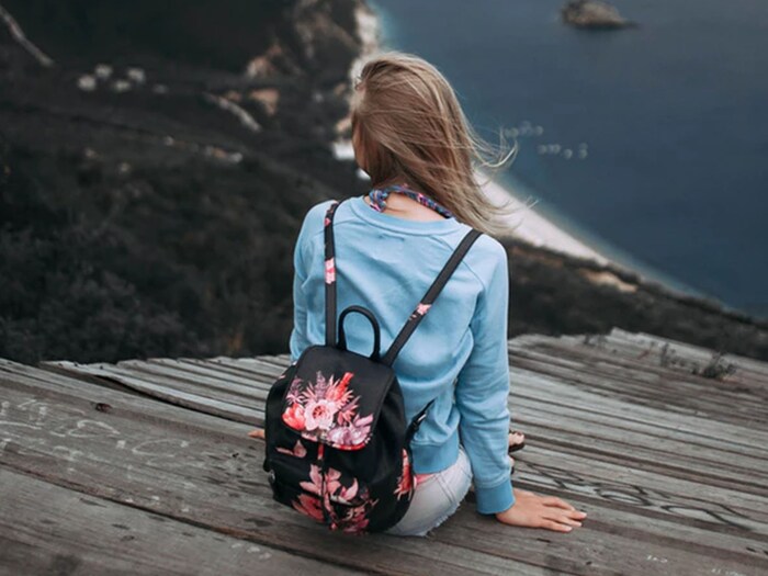 girl dressed in blue with a black backpack and a blond hair watching at a high point