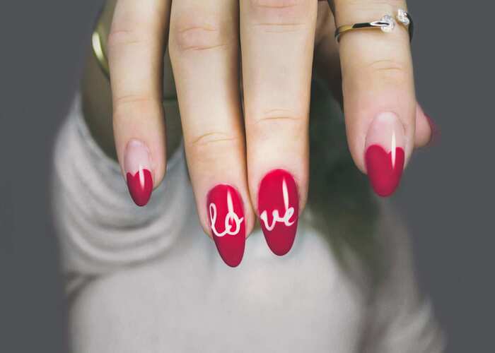 attract love woman's hand with long nails with red nail polish and a love written across them