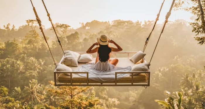 woman in a white dress with a sun hat on in a large swing overlooking the jungle