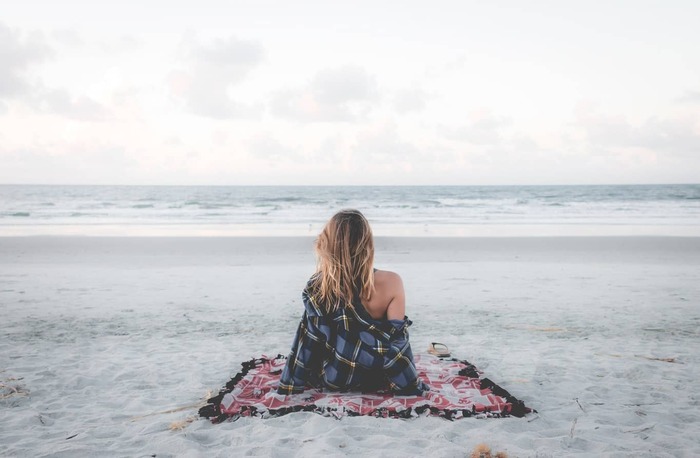 lonely woman on the beach sitting on a towel looking at the sea in the distance