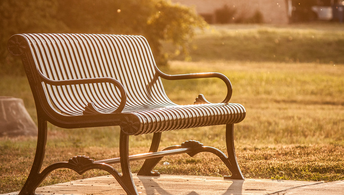 lonely outdoor bench in a park into the sunlight with a grass field in the background