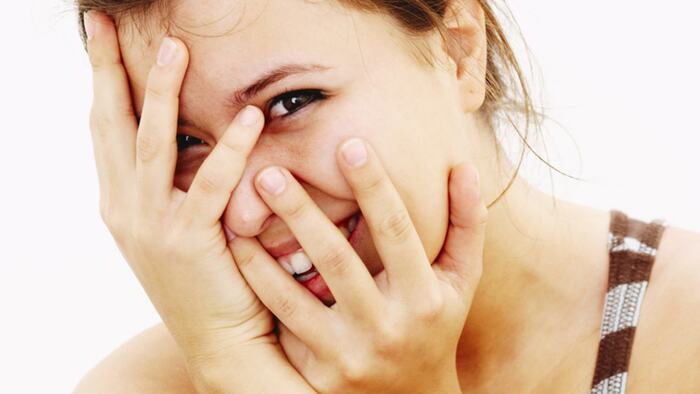 woman hiding her face with her hands smiling and looking at the camera