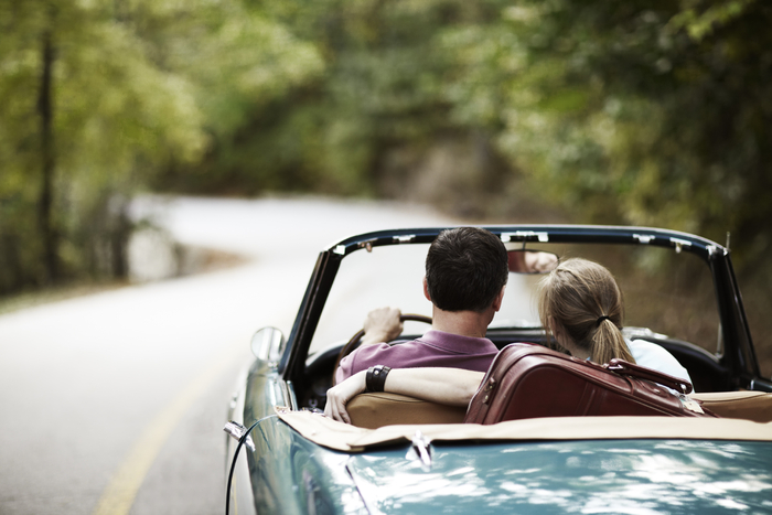 a couple driving a cabrio on a forest road in a retro car