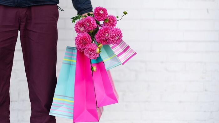 man in dark pants holding a bunch of paper bags and pink flowers