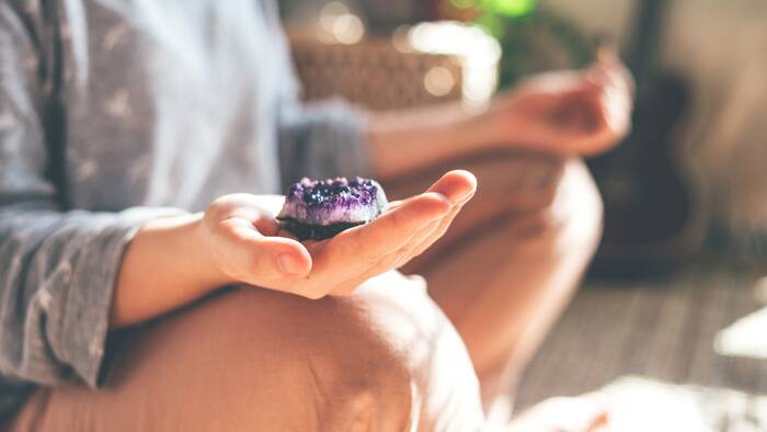 crystal healing woman sitting and meditating with a purple amethyst in her hand