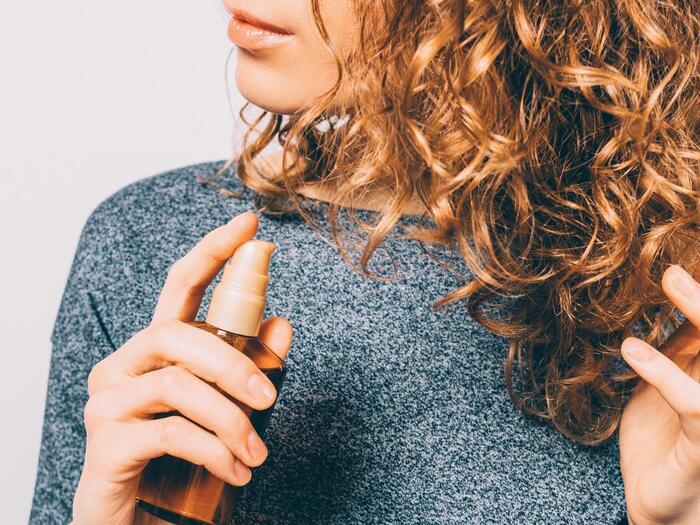 blond woman in gray shirt spraying her tight curls and applying product on them