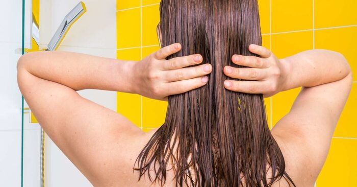 naked woman's back in the shower with her hands on her wet hair in a yellow and white bathroom wall