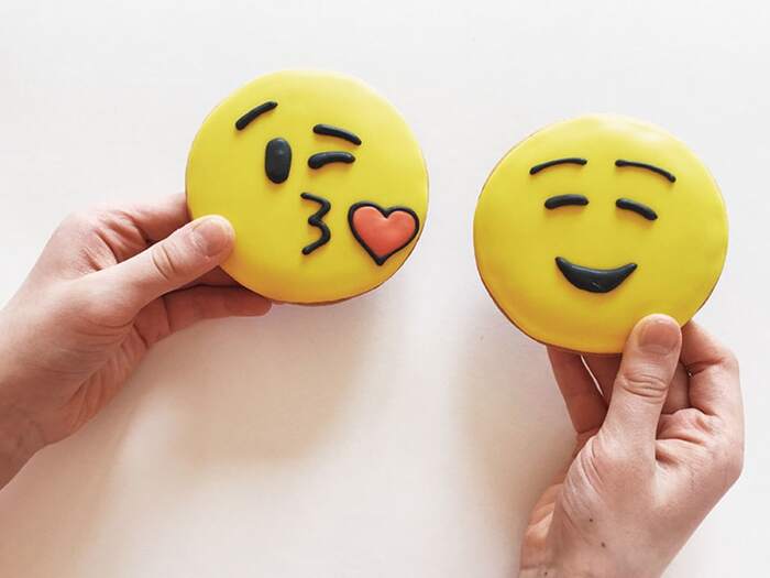 two hands holding cookies with yellow glazing with emoji faces in love
