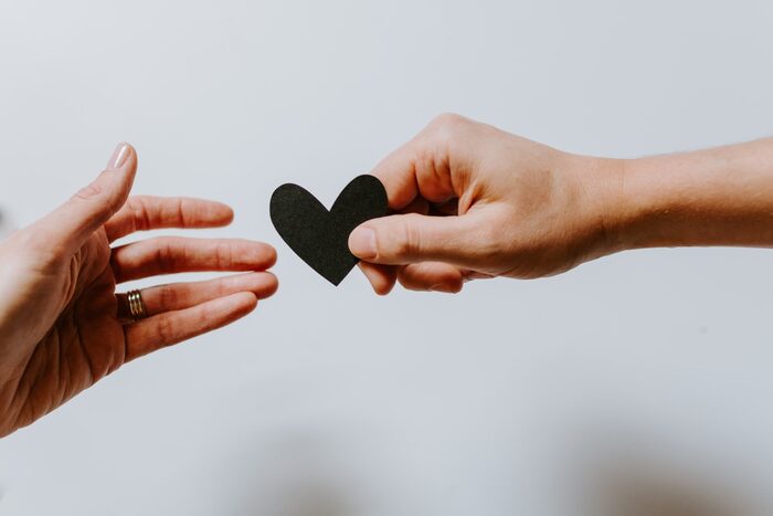 two hands exchanging a black paper heart on a white background