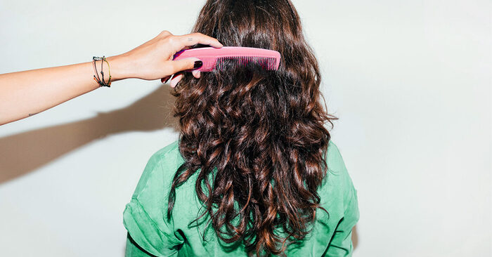 what does your hair need a hand combing curly hair of a woman dressed in a green shirt sitting with the back to the camera