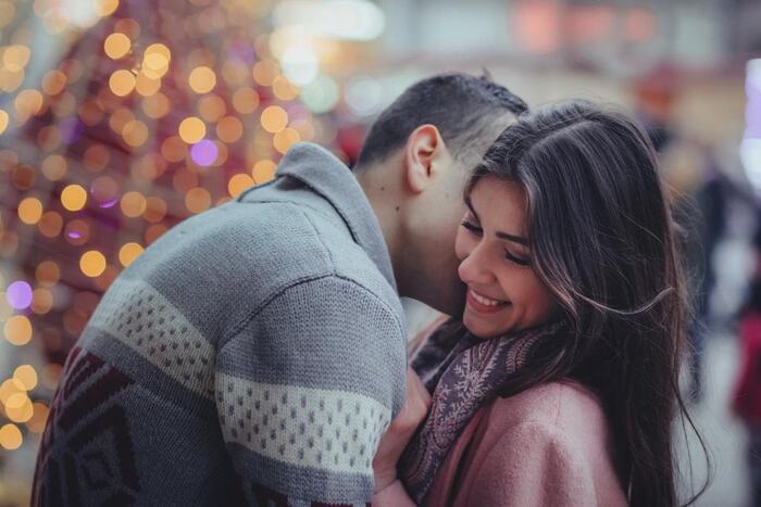 a couple kissing outdoors man in a sweater and a woman in a pink coat with a scarf