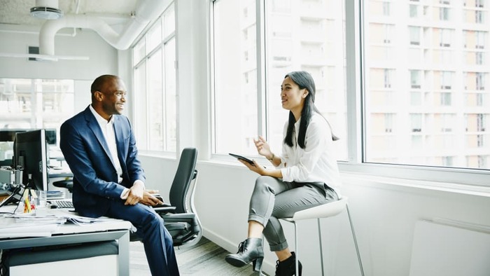 great resignation a man and a woman sitting in a white office space next to a window speaking to each other and smiling