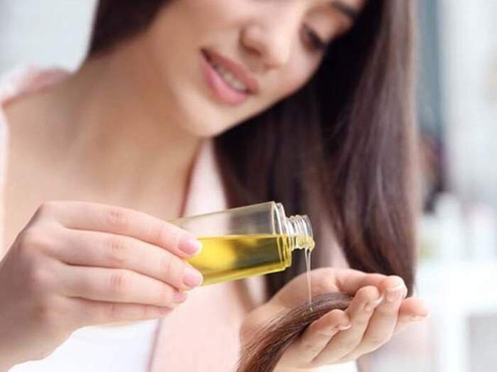 hair care woman with long black hair applying oil on the ends of her hair and smiling