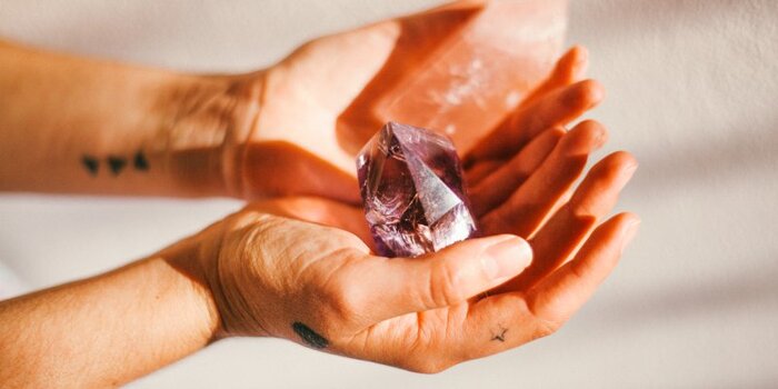 healing with crystals two hands holding a purple crystal at sunlight