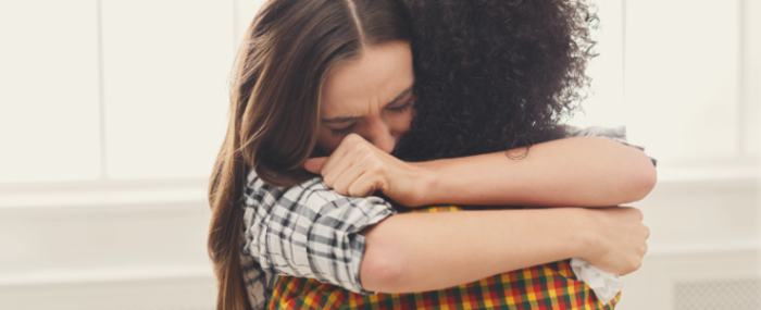 two women dressed in shirts hugging on a white background 