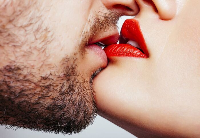 woman with a beard kissing a woman with red lipstick passionately