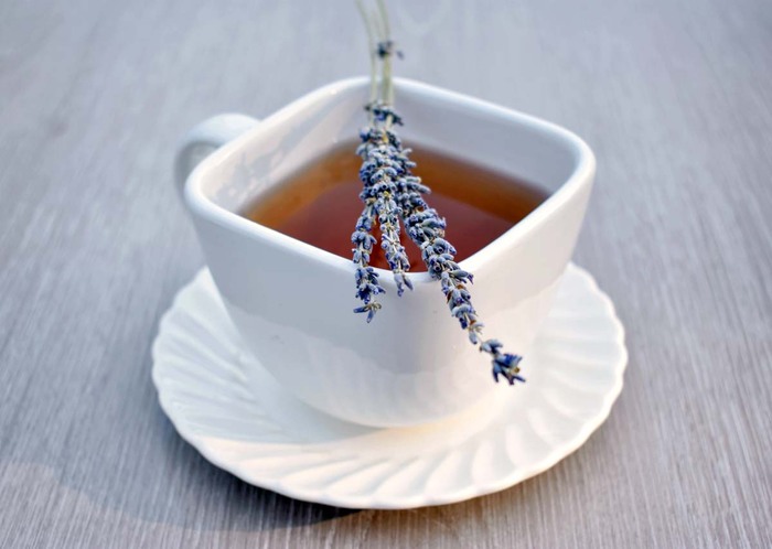 white tea cup on a grey table with lavender tea and a lavender flower on it