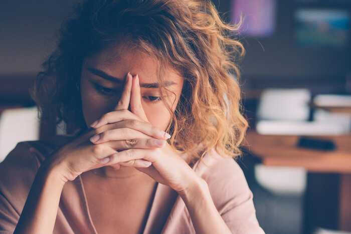 woman with curly hair sitting indoors thinking with her hands in front of her face