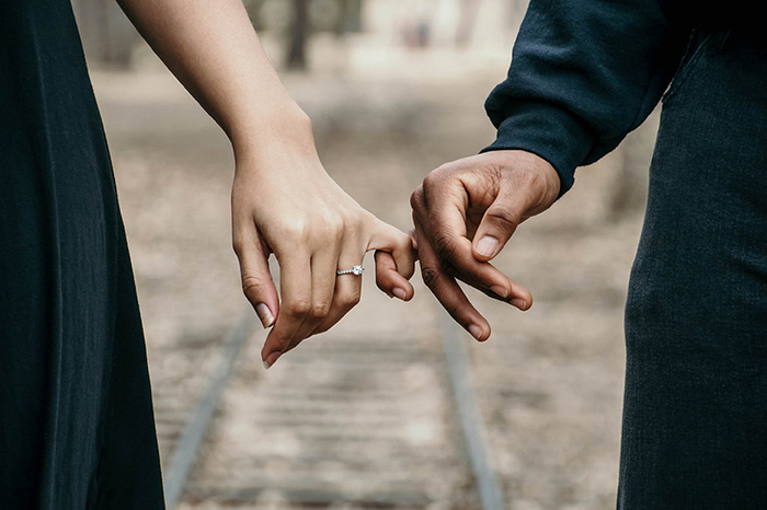 woman and man in black clothes holding hands walking on a train tracks together