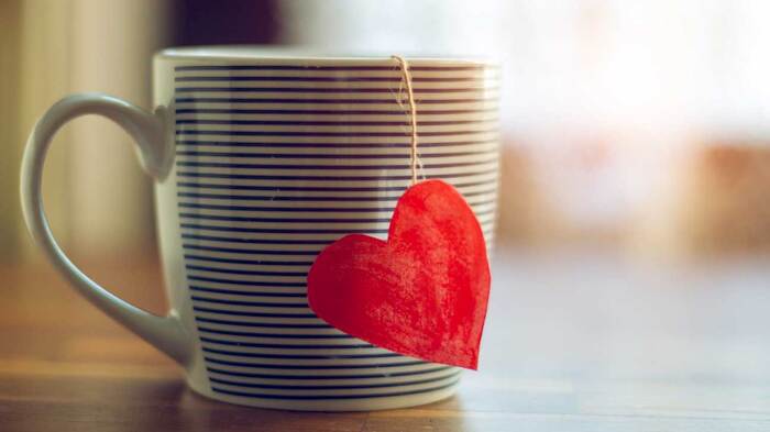 striped tea cup with a red heart hanging on one side on a table with the light coming through a window in the background