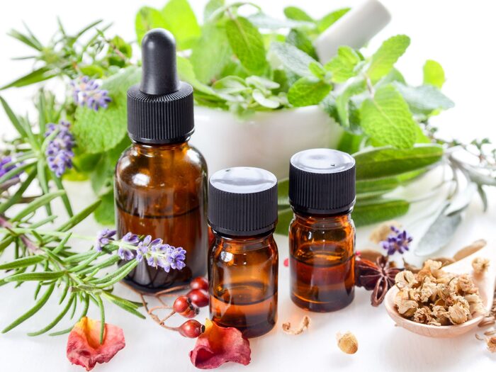 aromatherapy oils in brown bottles and green herbs in the background with rosemary mint cloves and rose petals