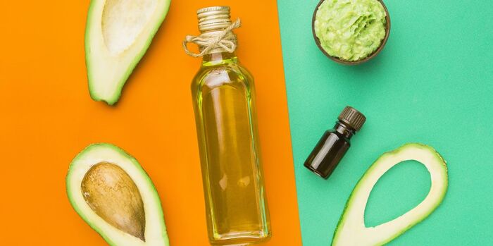 natural moisturizer oil in a glass bottle with avocado halves scattered around on an orange and green background