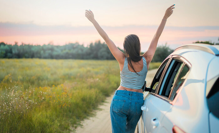 the back of a woman bending on a car on the road in the middle of nature